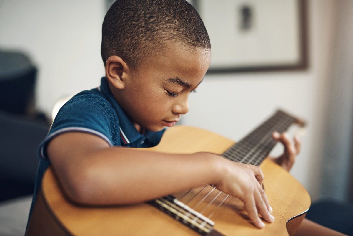 Young boy trying to play acuostic brown guitar