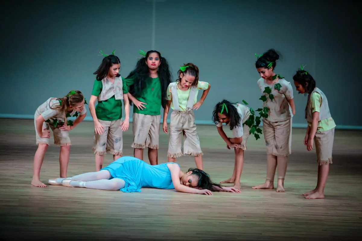 Children surrounding a fellow actress who has fallen asleep on the ground