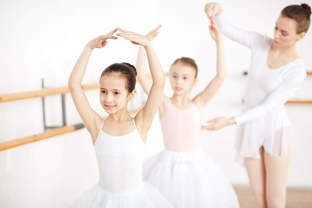 Twochild ballerinas being postion by teacher and their all wearing white