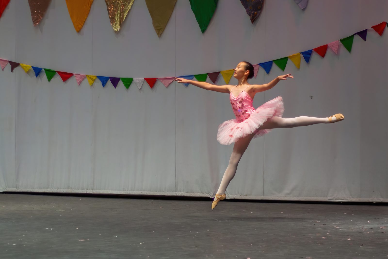 A girl in a pink tutu jumping and posing in a ballet pose