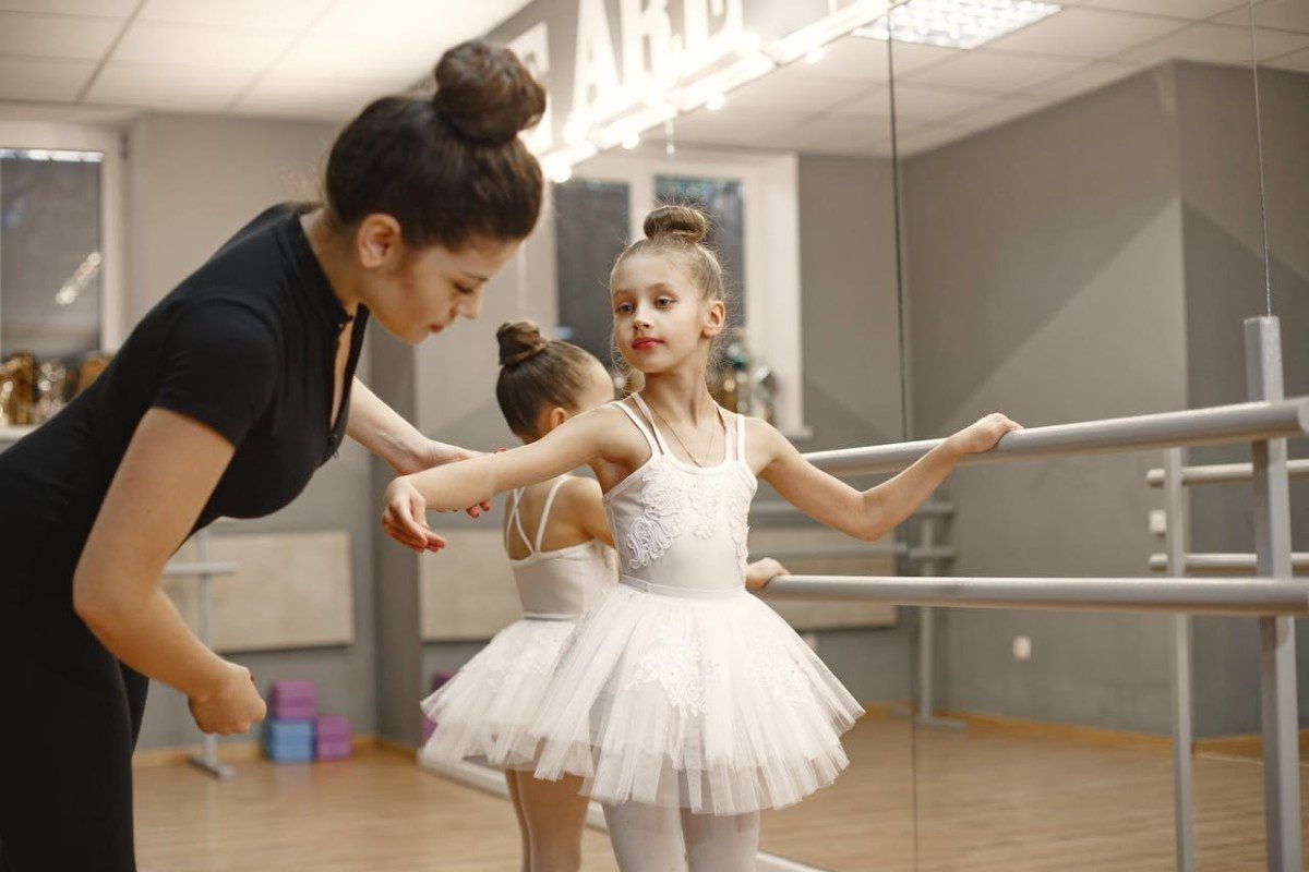 Two young ballerinas being taught how to stand by instructor