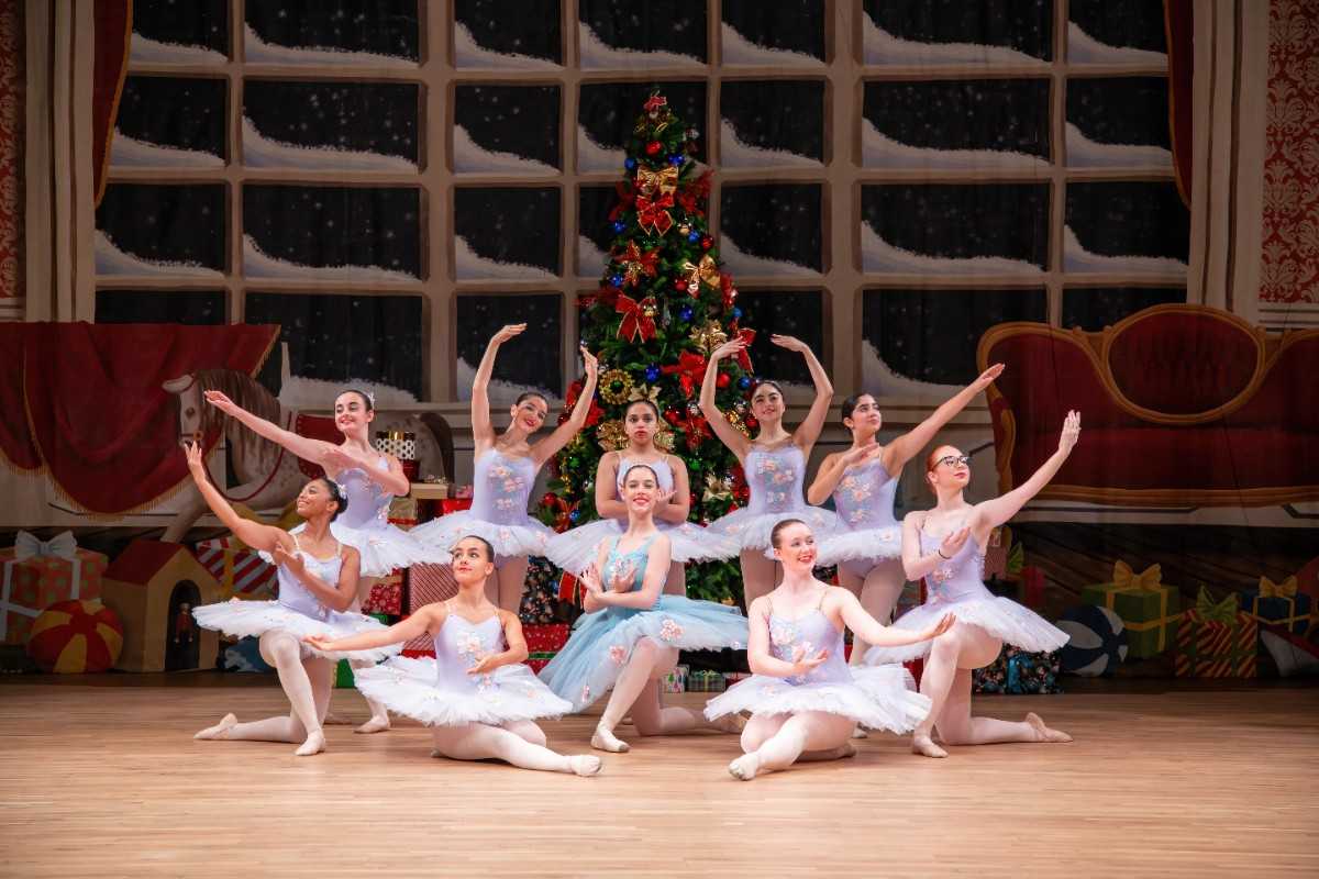 balletinas in a pose behind large christmas tree