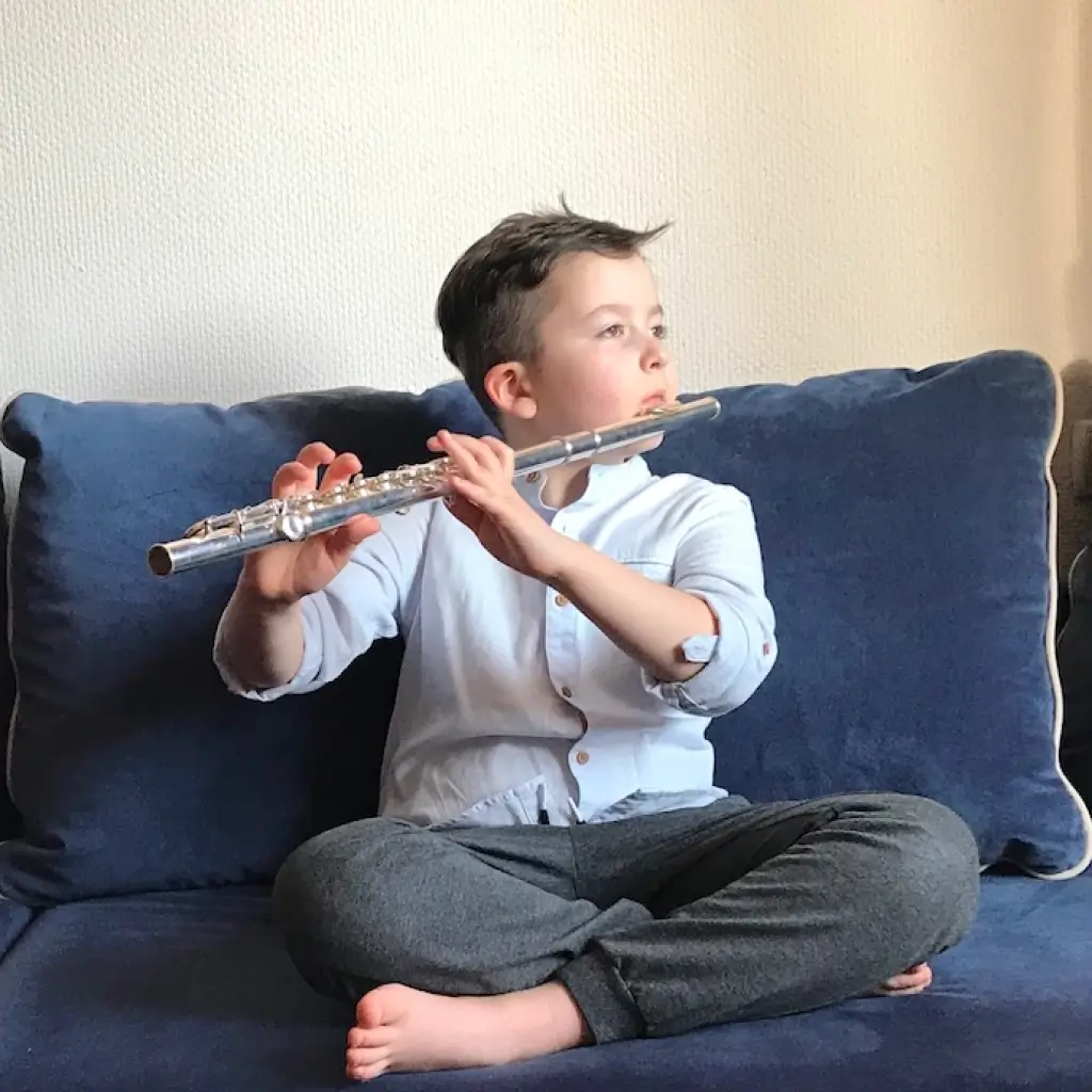 Little boy sitting on the couch and playing the flute