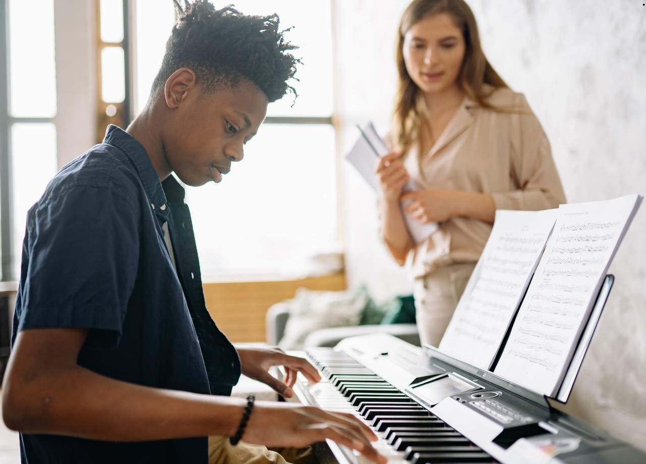 Young boy playing piano while teacher looks on