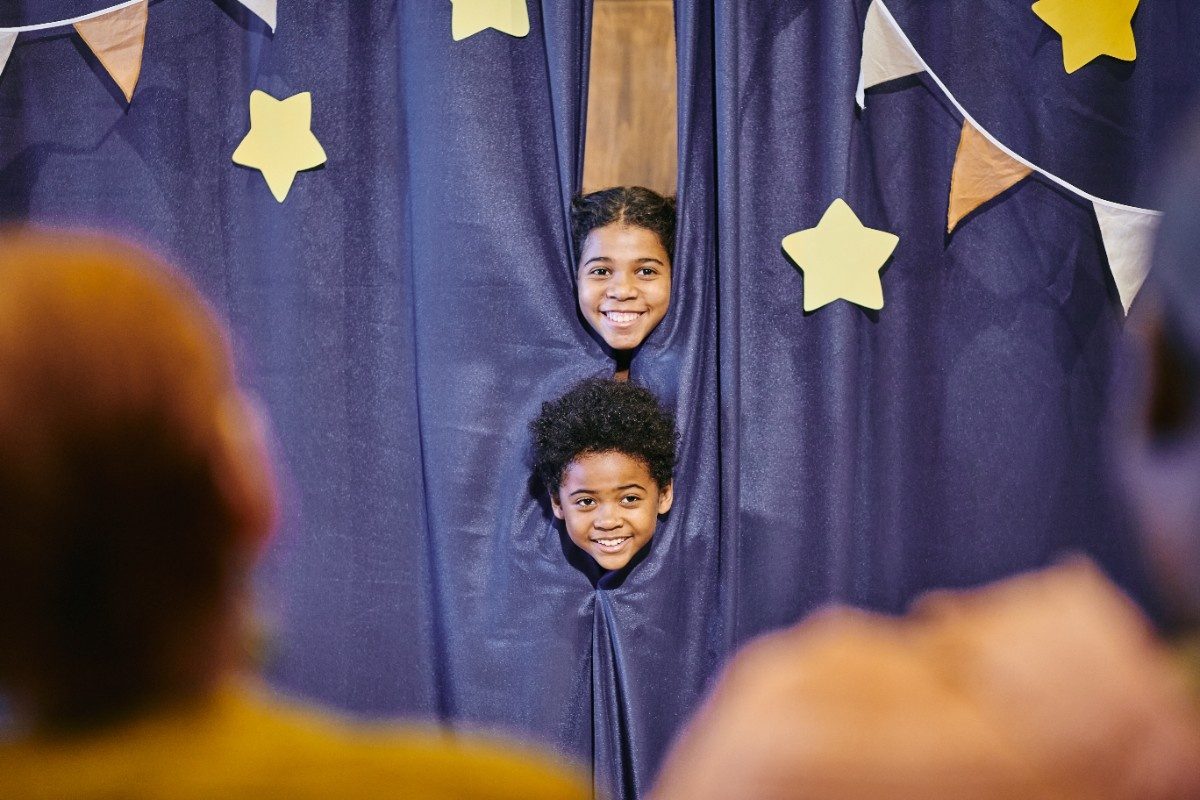 Two children peeping on stage as they get ready to perform