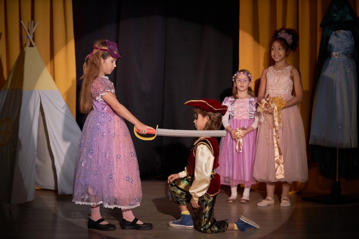 Girl on Stage in School Play as boy is knighted by the girl
