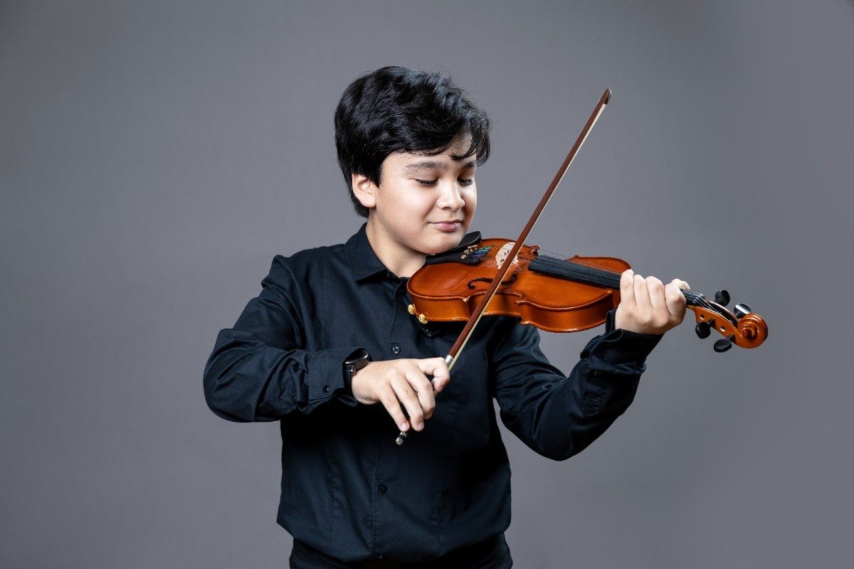 A boy wearing black playing the violin