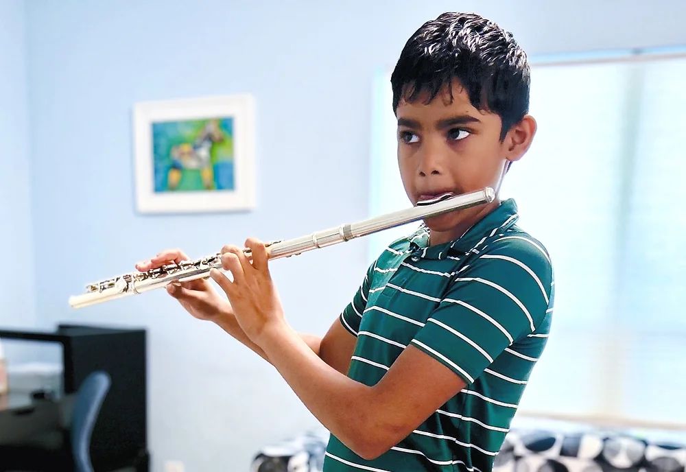 Young boy playing flute while focusing on reading music sheet