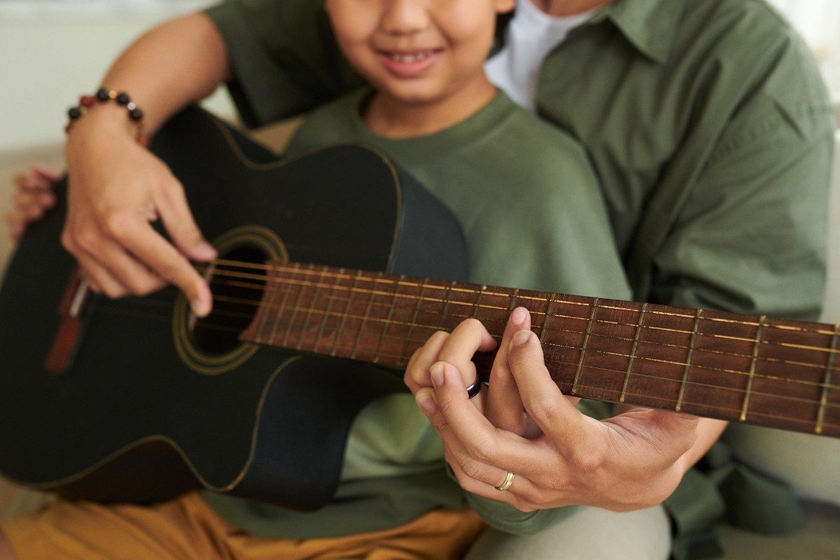 Father Teaching Son Playing Guitar as child smiles
