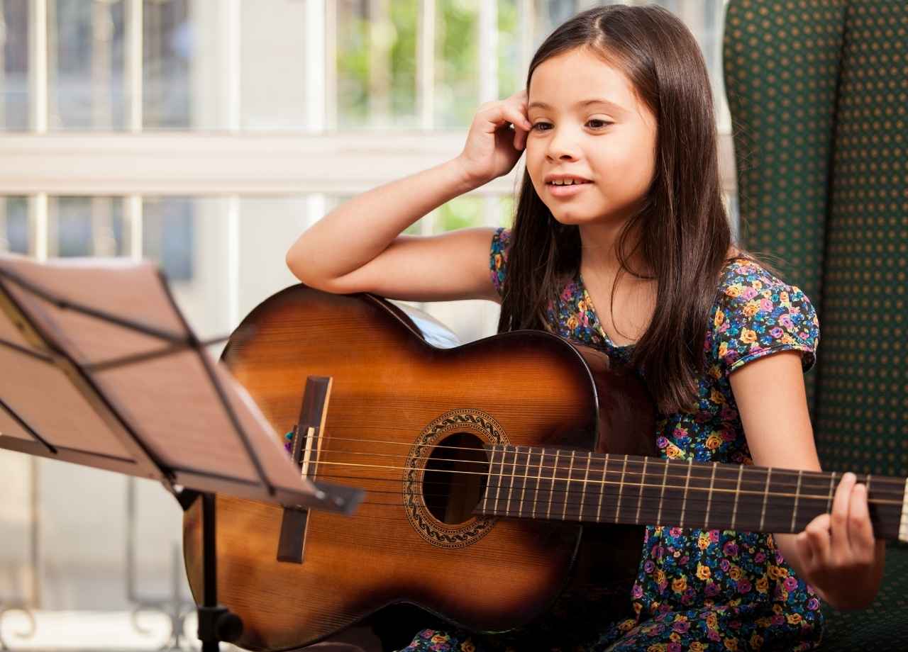 Little girl holding a guitar and looking at music sheet