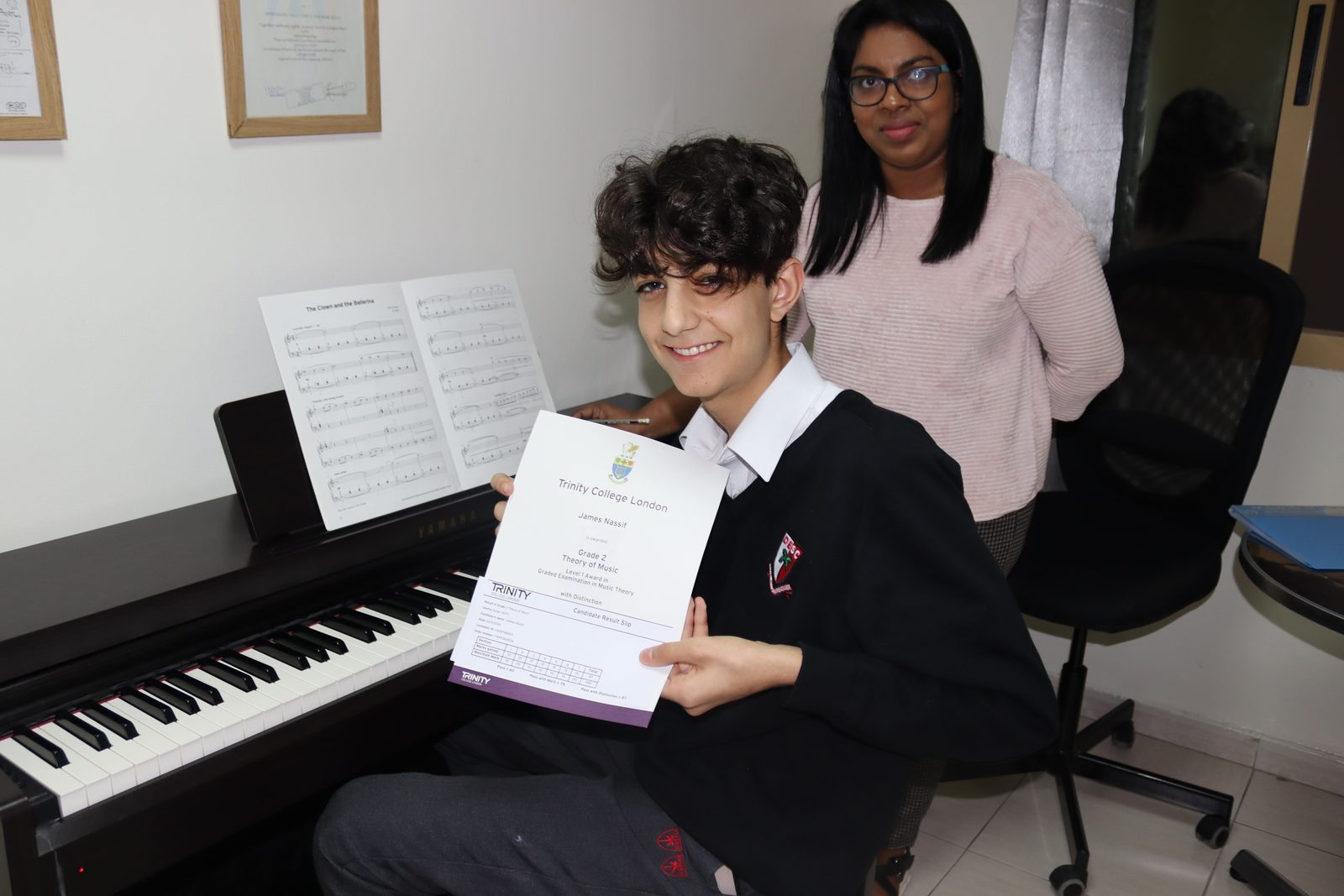 A child and his piano tutor sitting whilst child holds certificate to the camera