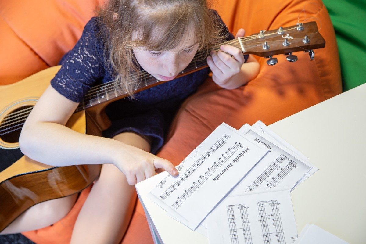 A little girl learns to play the guitar by sheet music