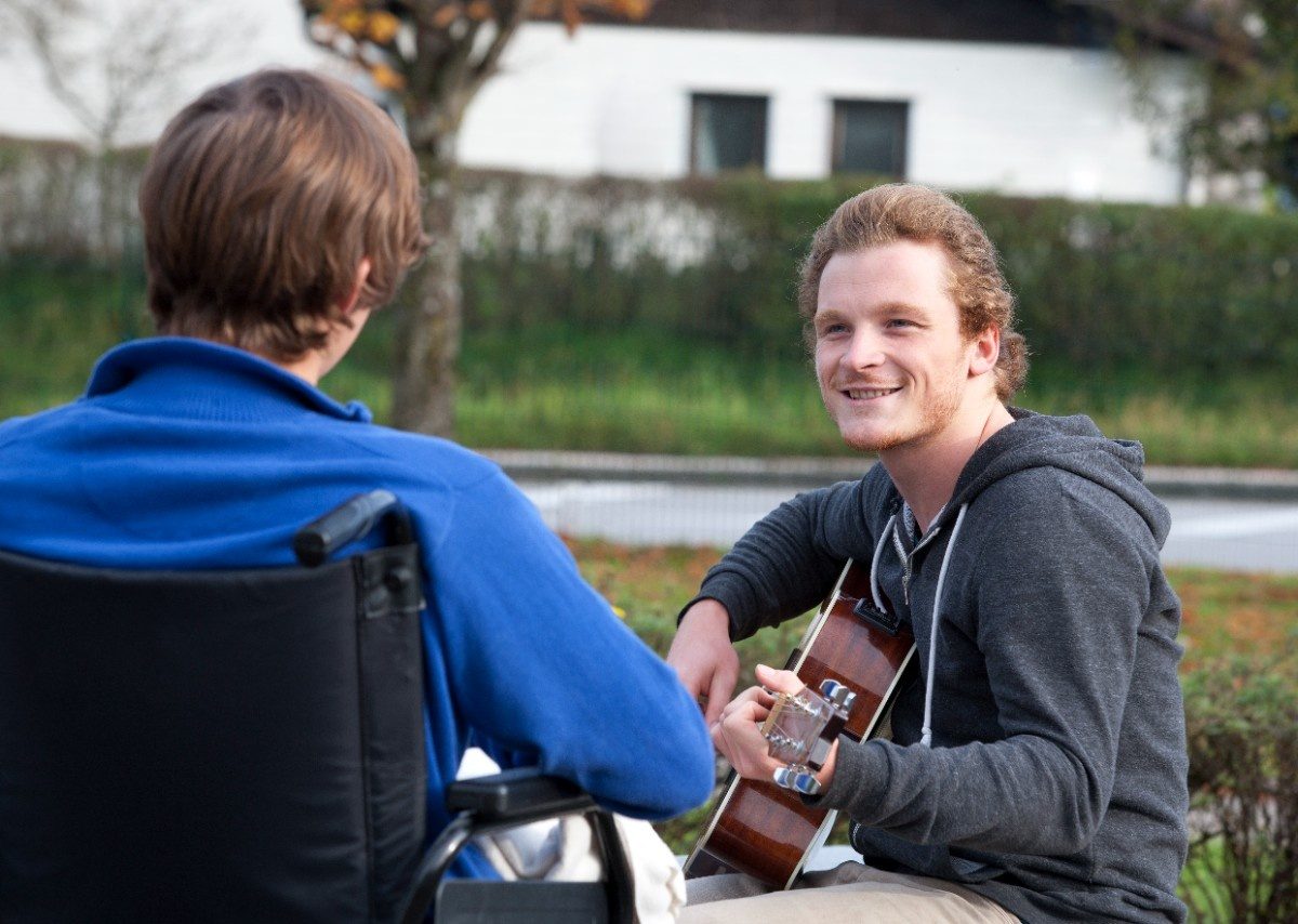 Young wheelchair user listening guitarist