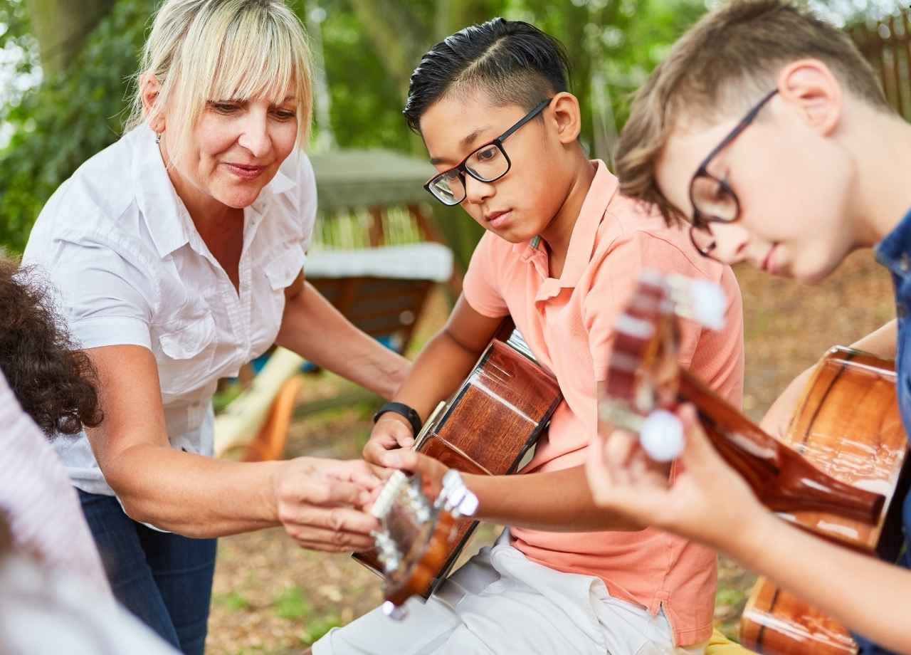 An older woman trains young boys on how to hold and play a guitar