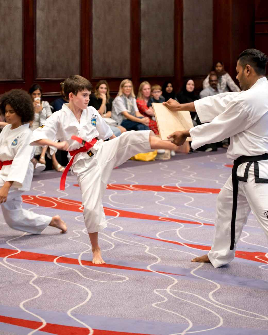 Young Taekwondo red belt kicking a board held up by his instructor