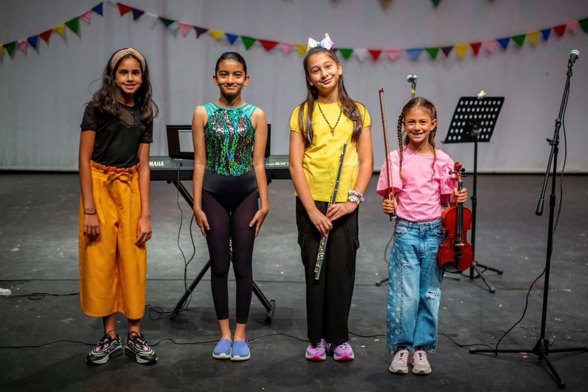 4 young girls smiling with two of them holding musical instruments