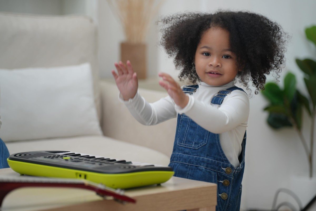 young girl smiling with hands raised with a keyboard in front of her