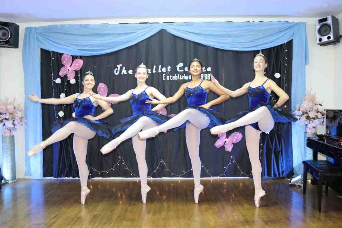Four women wearing blue ballet attire with one leg up