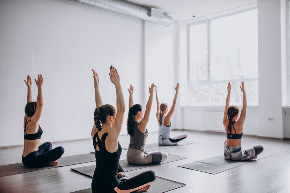 Women sitting in a yoga classon yoga mats with their hands raised up