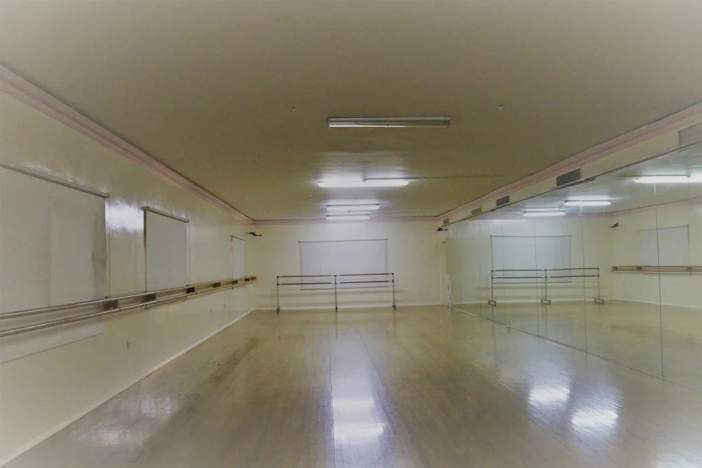 A dance studio with a polished wooden floor, barres and mirrors