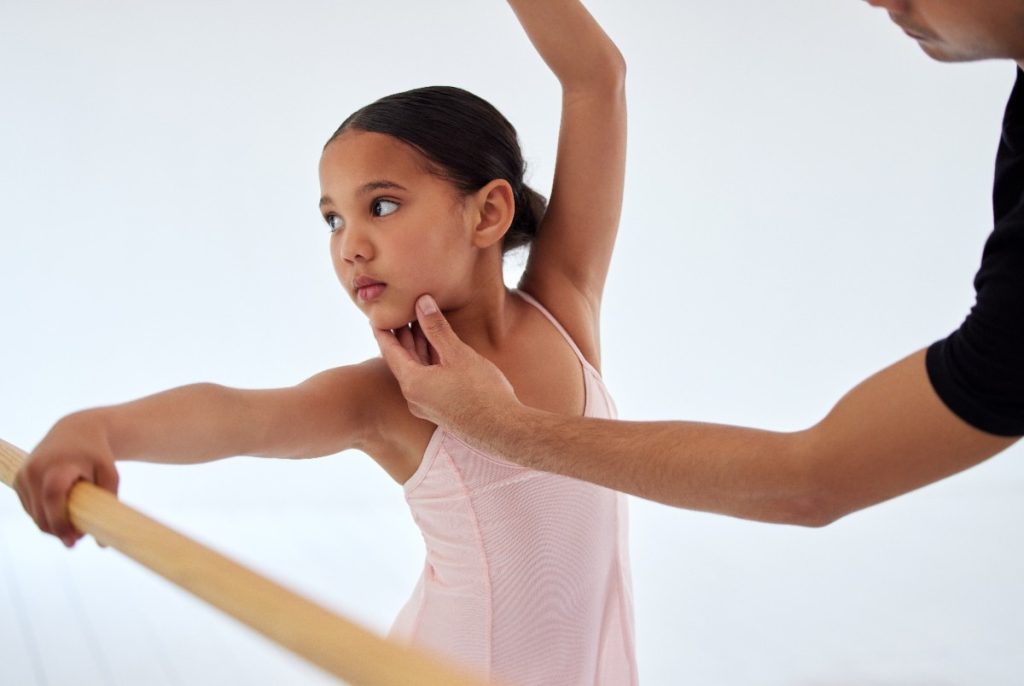 A child in pink tutu in a ballet class with her position being corrected
