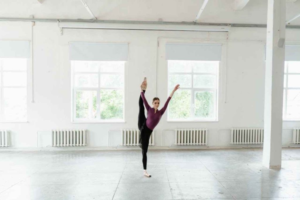Woman in ballet studio, she is lifting one foot above her head