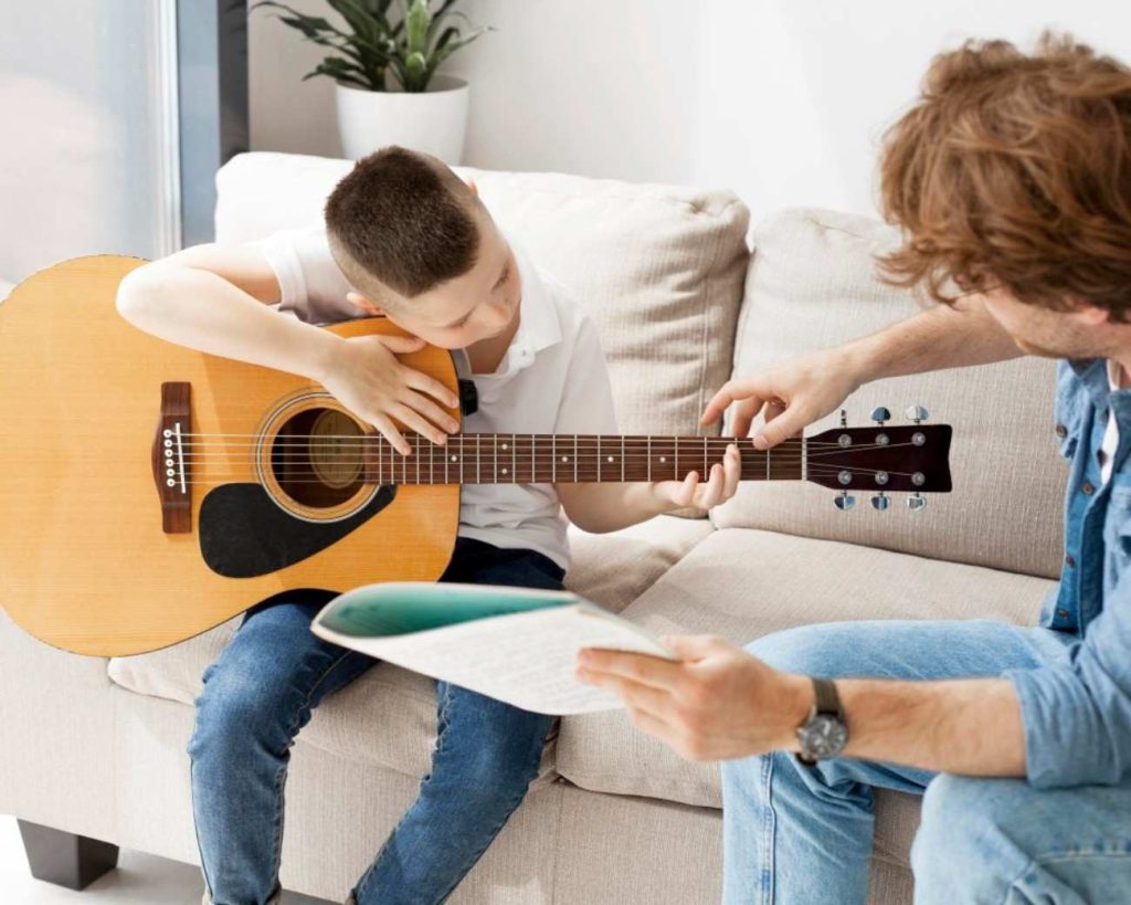 Young boy holding guitar as he is taught how to hold and play it by male instructor
