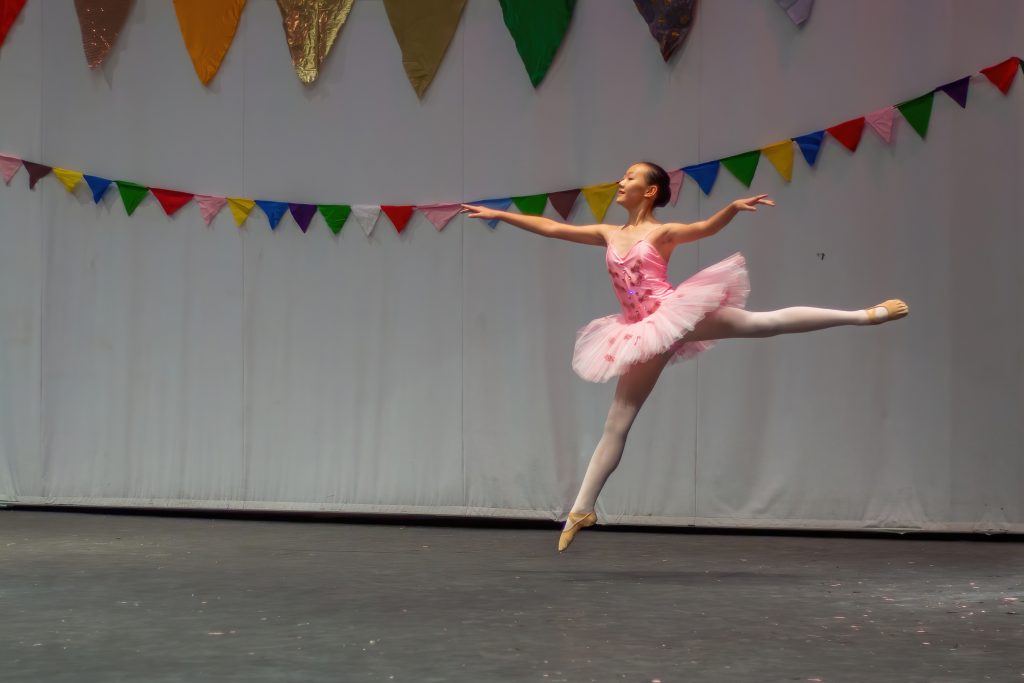 A girl in a pink tutu jumping and posing in a ballet pose
