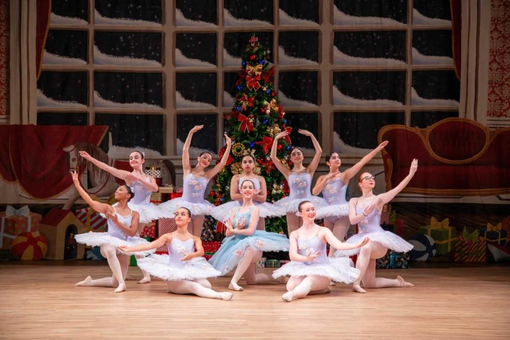balletinas in a pose behind large christmas tree