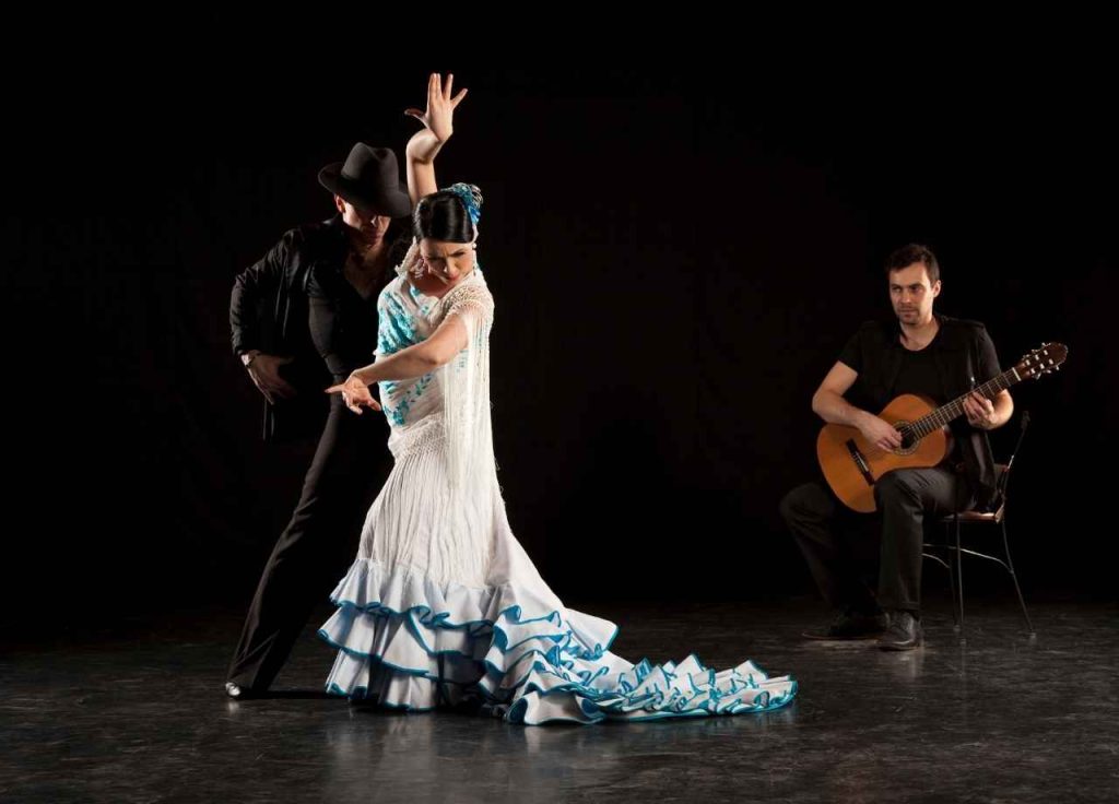 two flamenco dancers and a man sitting whilst playing the guitar. 