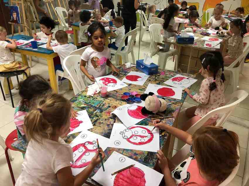 Children sittings on desks busy with painting in Arts and Crafts