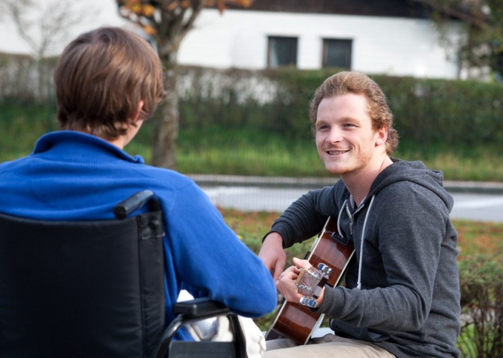 Young wheelchair user listening guitarist